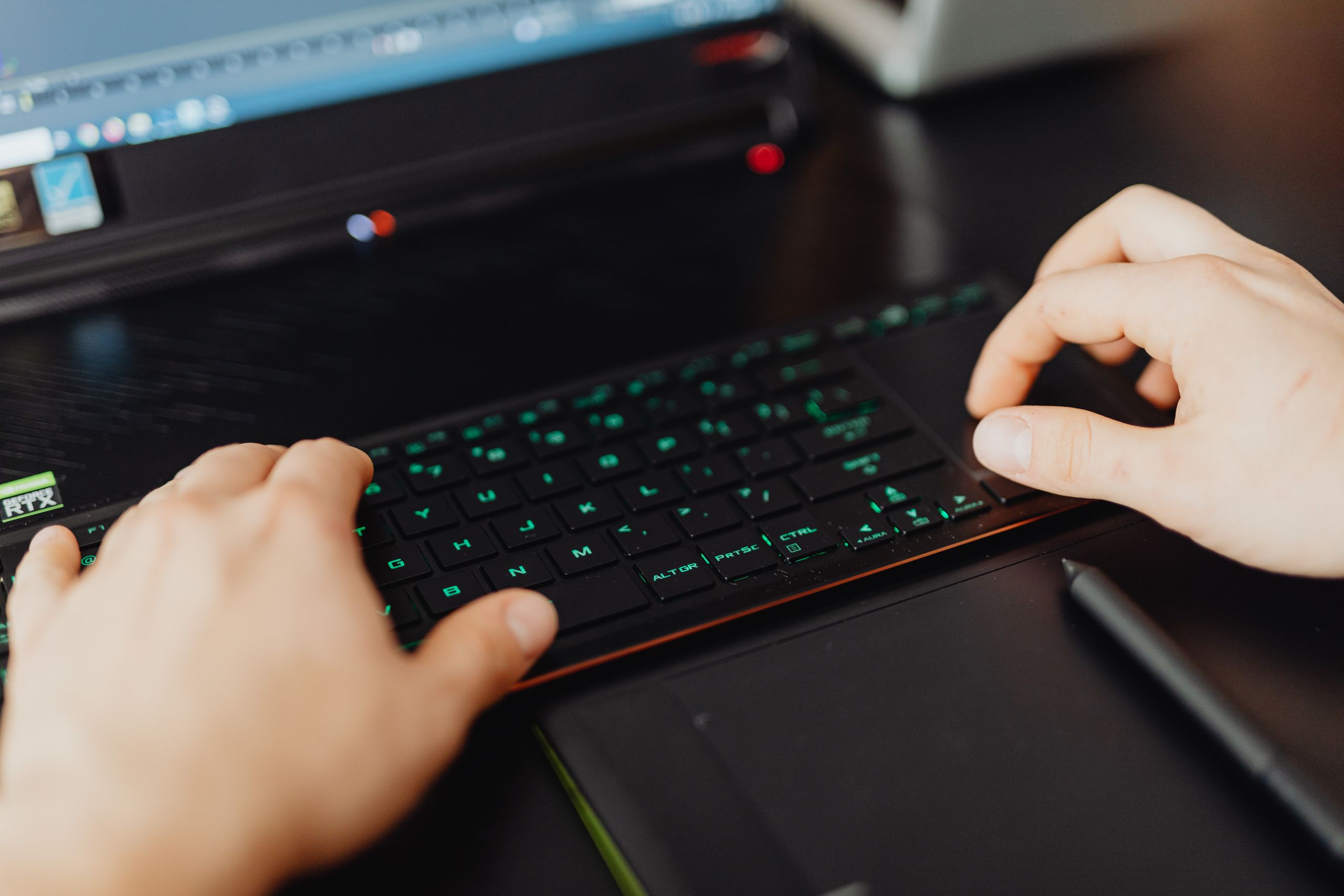 Closeup of hands typing on an RGB keyboard in a modern office setting.